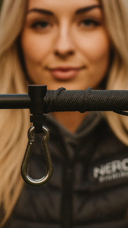 Close-up of weigh clip and carabiner attached to a bankstick with a blurred woman wearing a black jacket in the background.